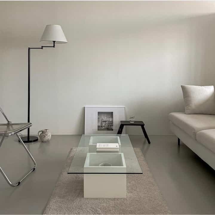 A simple living room in white and monotone shades, featuring a modern sofa and glass coffee table with a calm atmosphere