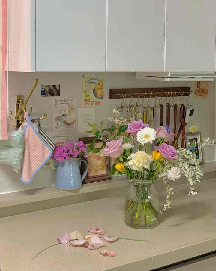 White-toned kitchen space featuring a vase with mixed flowers and hanging kitchen utensils, creating a warm and cozy atmosphere