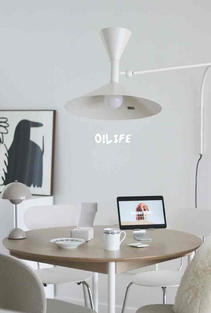 白い壁とナチュラルな木目調のダイニングテーブルがあるモダンなダイニング、エルメスの食器とテーブルランプが配置された印象的な空間