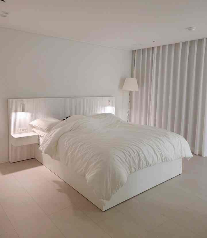 White-toned bedroom featuring a cozy hotel-style bed, nightstands with lamps, and a simple, warm atmosphere