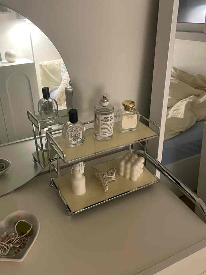 Ivory-toned bedroom vanity with an arched mirror, neatly arranged perfumes and objet candles in a simple setting