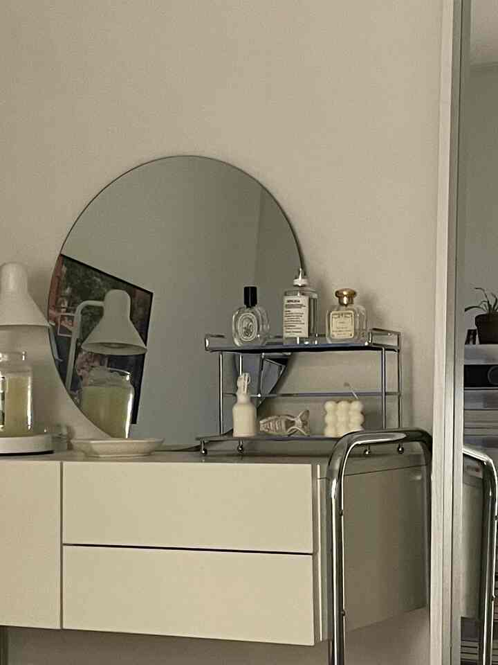 A simple and modern space featuring a white and silver-toned mirror and vanity with decorative objects