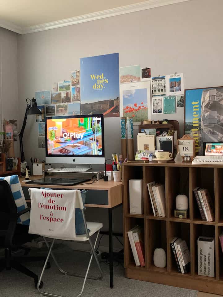 Natural tone home office with brown wooden desk and bookshelf, decorated wall featuring various posters and photos