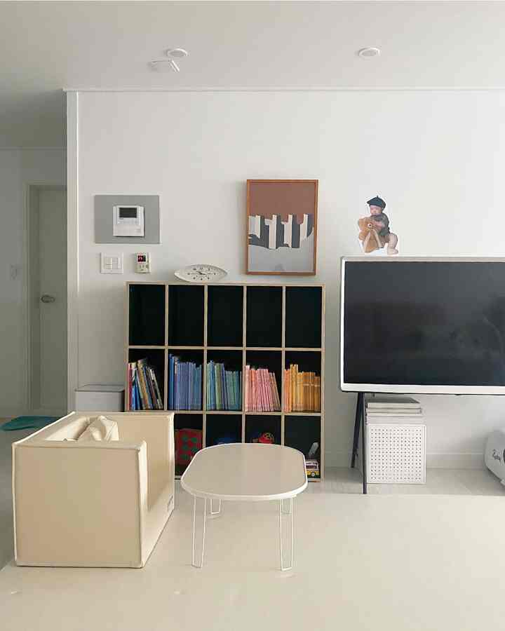 白とベージュの落ち着いたリビング、子供向けの本棚と低いテーブルが配置されたシンプルで心地よい空間