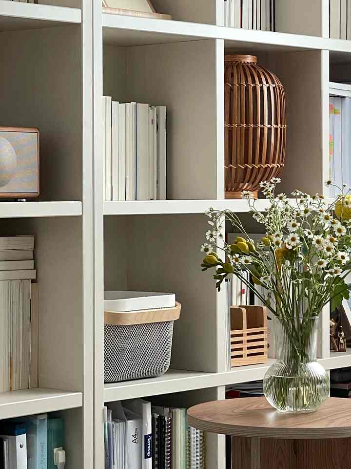 Natural-tone study with white bookshelf, wood tone table and a vase with flowers creating a calm atmosphere