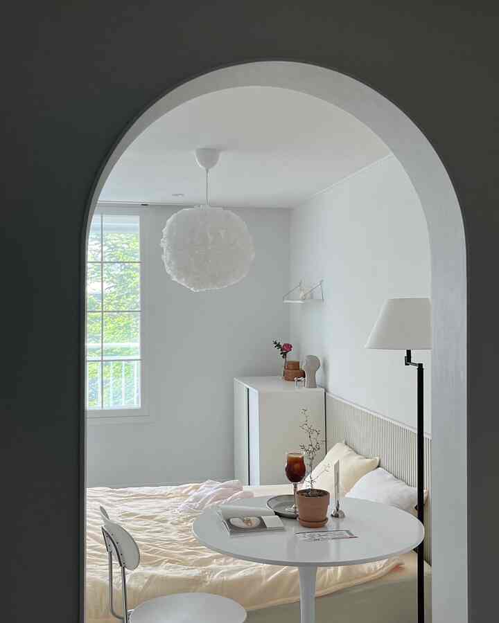 白とベージュのトーンの寝室、整ったベッドとペンダントライト、小さな丸テーブルが調和するナチュラルモダンな印象的な空間