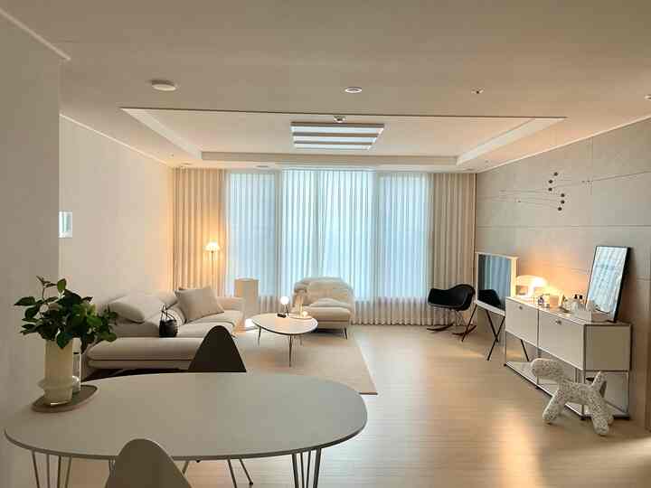 Modern living room in white and beige tones featuring sectional sofa, curtains, and floor lamps with a clean, bright atmosphere