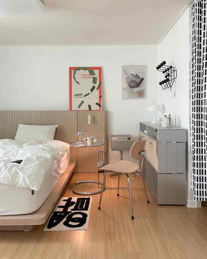 A wood tone and white bedroom featuring a mid-century modern bed, side table, framed posters with a simple modern atmosphere