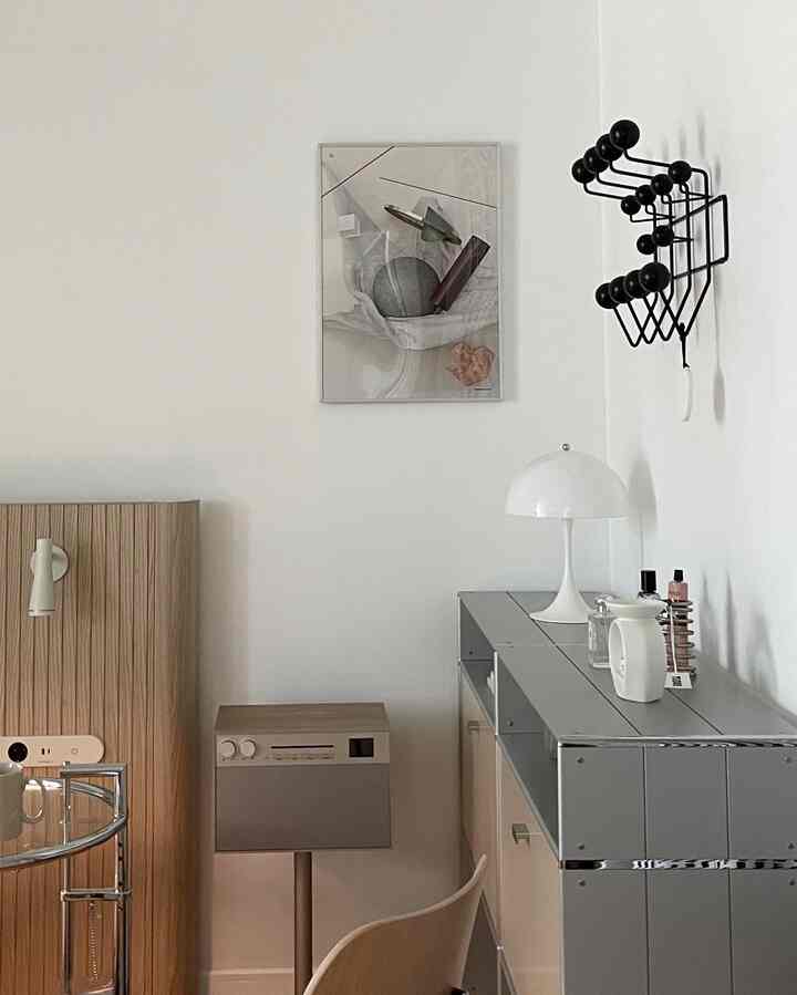 A simple Korean interior home office space blending white, gray, and wood tones, featuring a table lamp and picture frame.