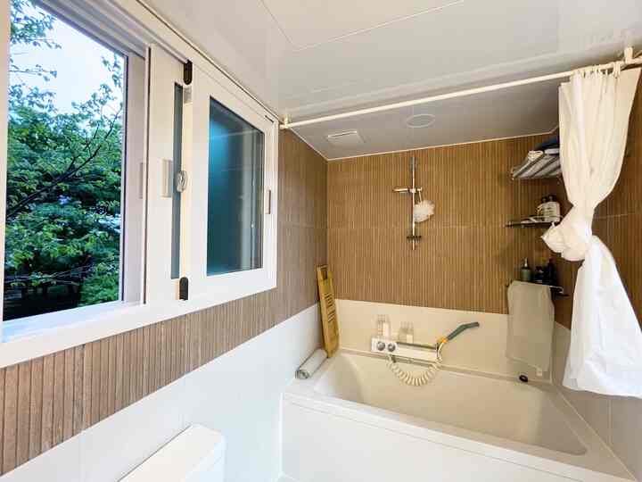 Natural brown tiled wall and white bathtub with curtains in a well-ventilated bathroom space
