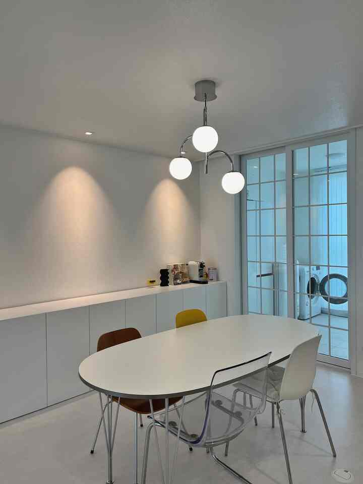 White-toned dining room with colorful chairs and pendant lights creating a clean, harmonious space