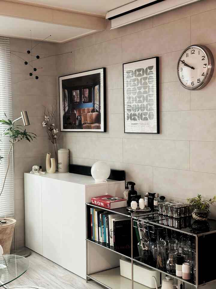 Natural-toned living room featuring white cabinets, modular shelving, wall art, and a clock in a modern interior
