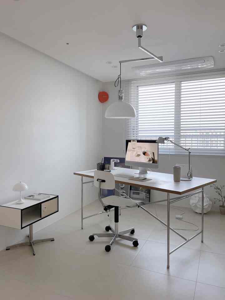 Bright minimalist home office with white walls and floor, featuring a simple desk and office chair in a well-lit room