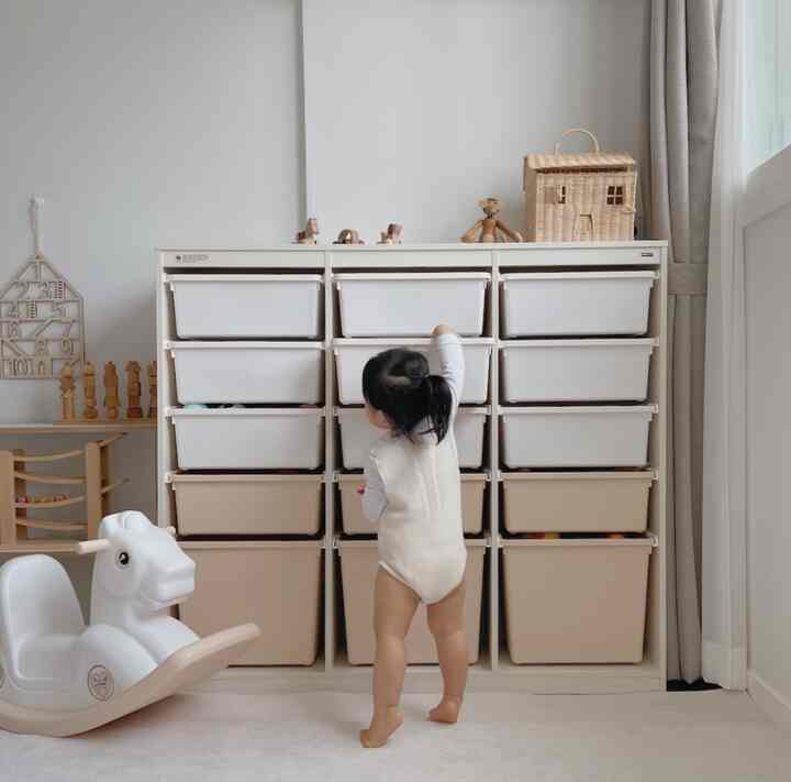 Bright beige and white kids' room featuring multiple storage bins and toys, with a child interacting with toy storage in a cozy space