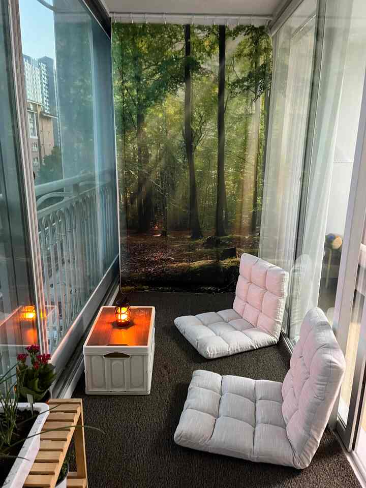 Beige and white toned balcony space featuring nature-themed curtains and floor cushions creating a cozy relaxation spot