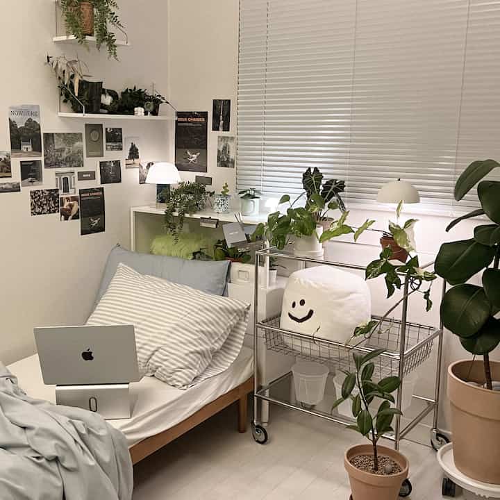 白い壁とブラインド、木目のベッドと多様な植物が配置されたコンパクトなミッドセンチュリーモダンスタイルの寝室空間