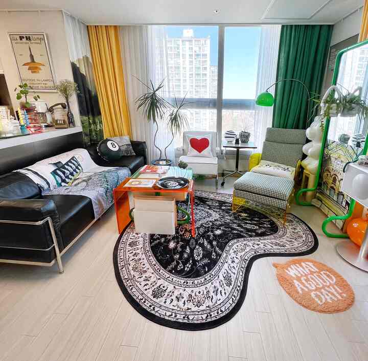 Bright living room with yellow and green curtains, white armchair and black leather sofa, highlighting a uniquely shaped black rug