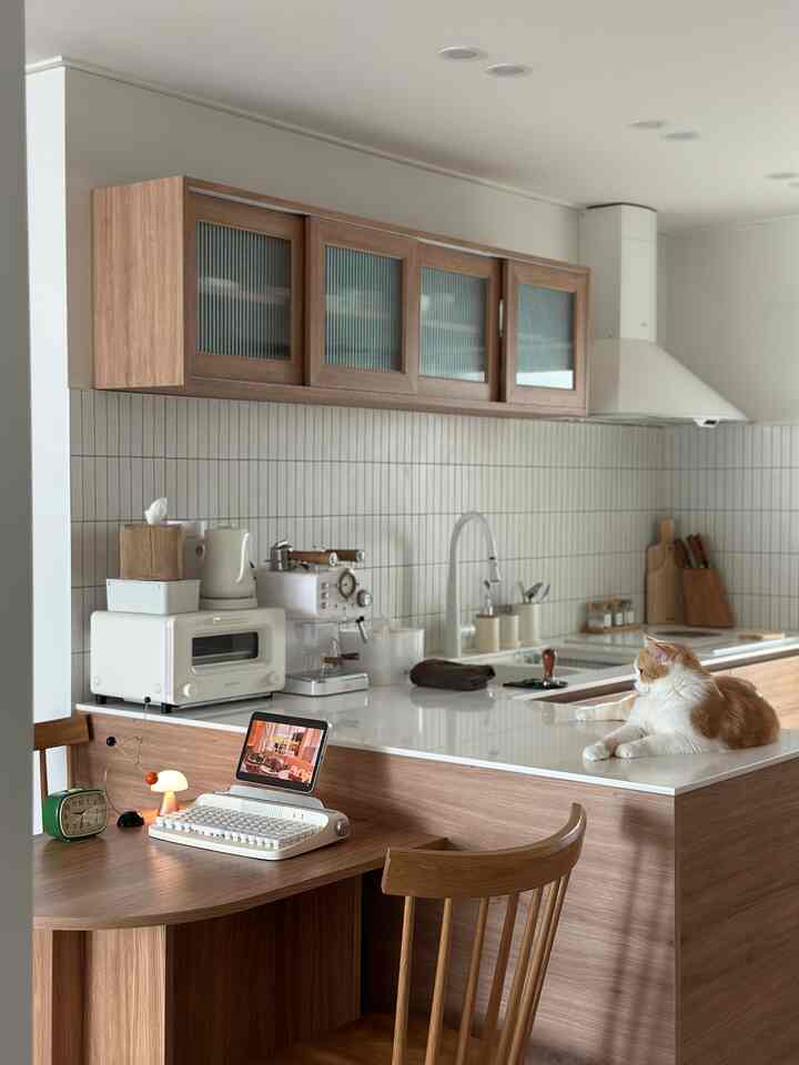 ナチュラルな木目調のキッチンとホームオフィスコーナー、カウンターにくつろぐ猫が印象的な空間