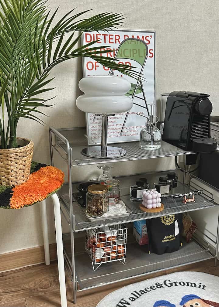 Natural tone compact studio apartment home cafe, featuring mesh rack shelf with Nespresso machine, plant, and stool in cozy interior