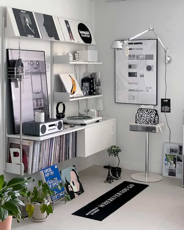 White and black toned compact music lounge featuring shelves with vinyls, wall sconce, and a minimalist rug