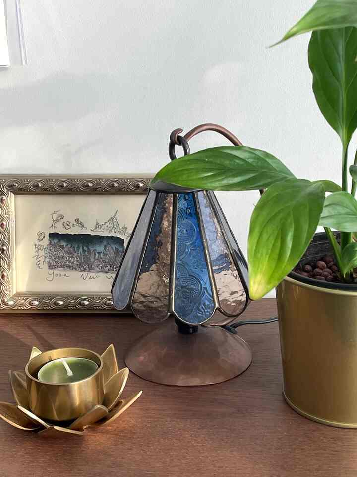 Gold and vintage toned decorative stained glass stand with candle and plant on cozy table setting