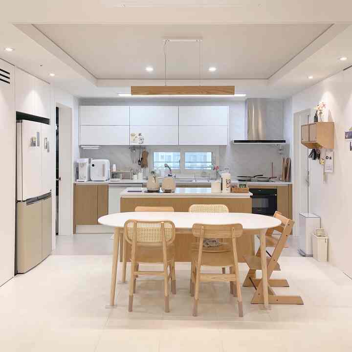 White and wood tone kitchen featuring natural furniture and a baby chair, creating a clean and minimal atmosphere