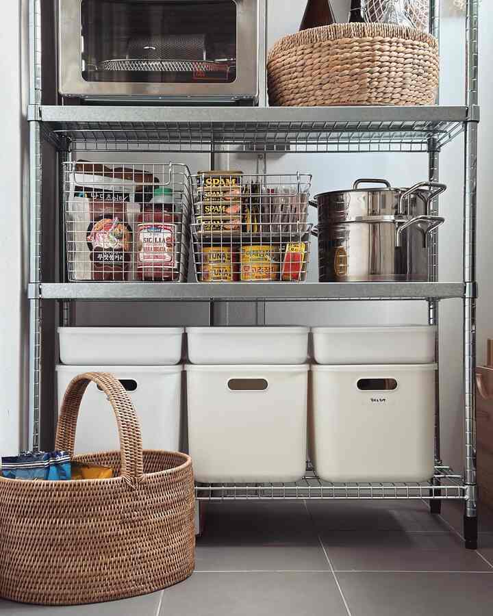A clean utility pantry featuring white storage bins and stainless steel shelves organized with wire baskets and living boxes