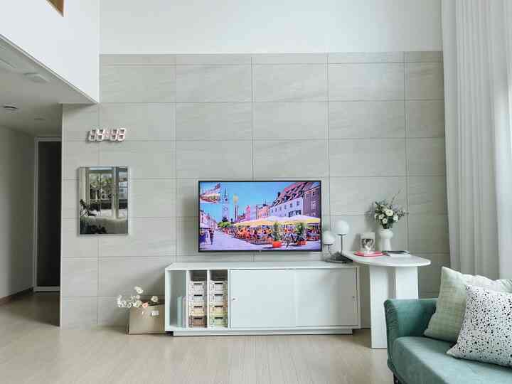 Modern and clean living room with white and gray tones featuring a green sofa, TV stand, table lamps, and vase decor