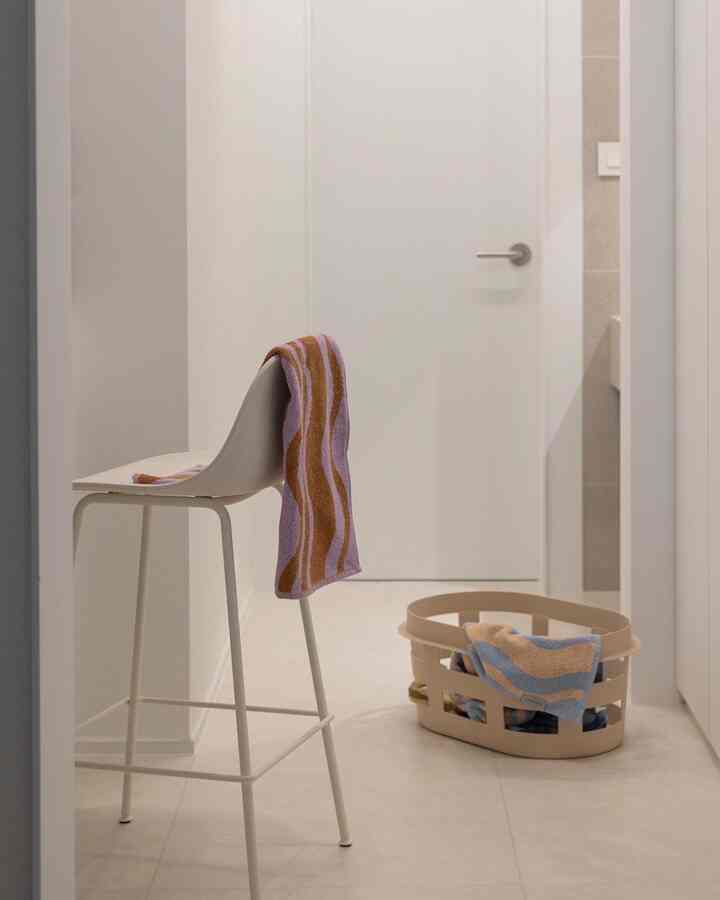 Beige and white toned bathroom featuring a stool and a towel basket with a practical atmosphere