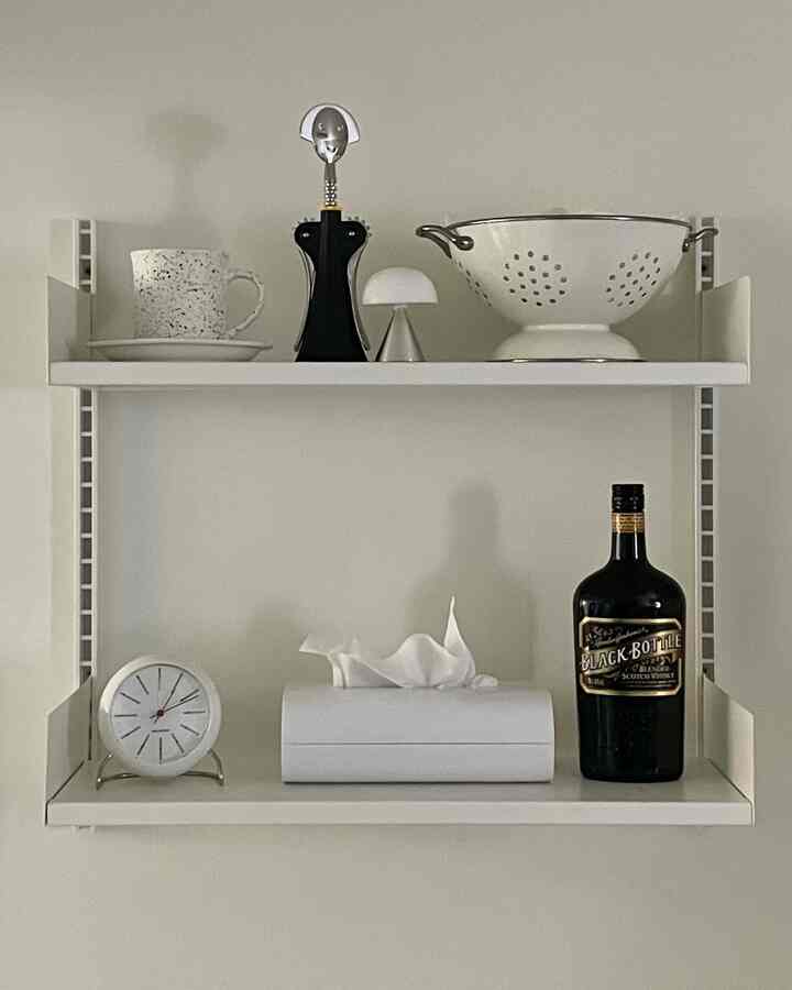 Modern kitchen shelf in white and black tones featuring various kitchenware and decorative objets with a clean arrangement
