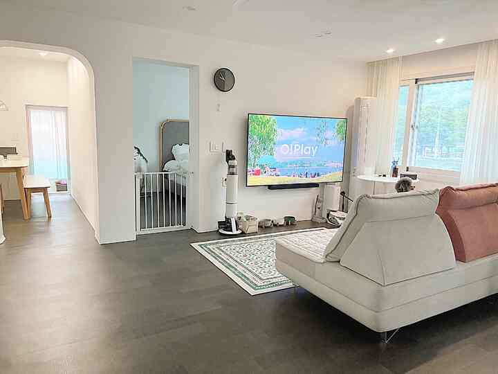 白とダークブラウンのトーンのモダンなリビングルーム、大きなソファと壁掛けテレビが配置されたシンプルで落ち着いたインテリア