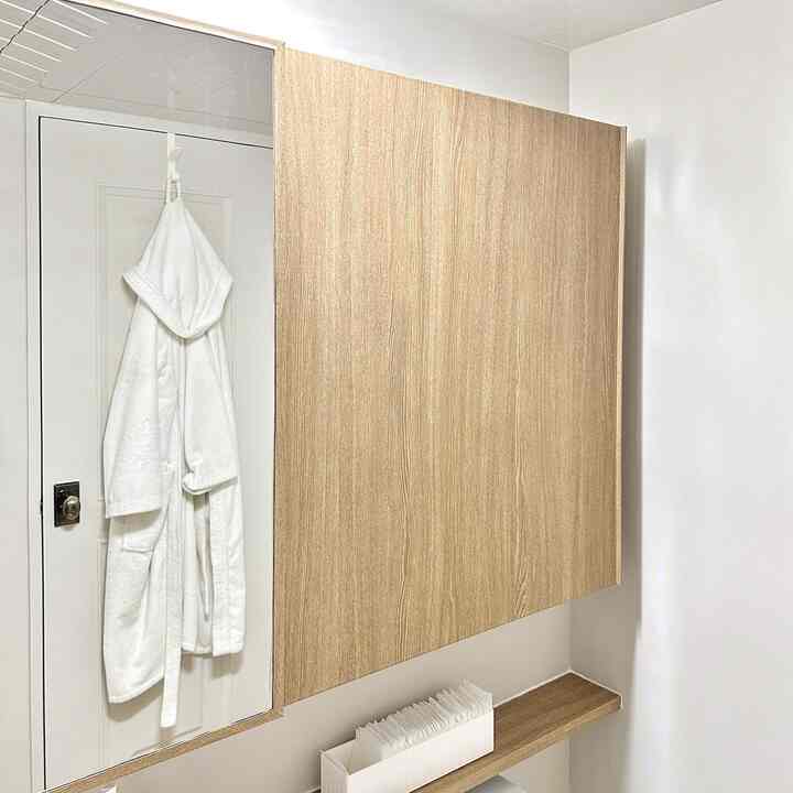 White and wood tone bathroom featuring wooden cabinet and white bathrobe, creating a clean and cozy atmosphere