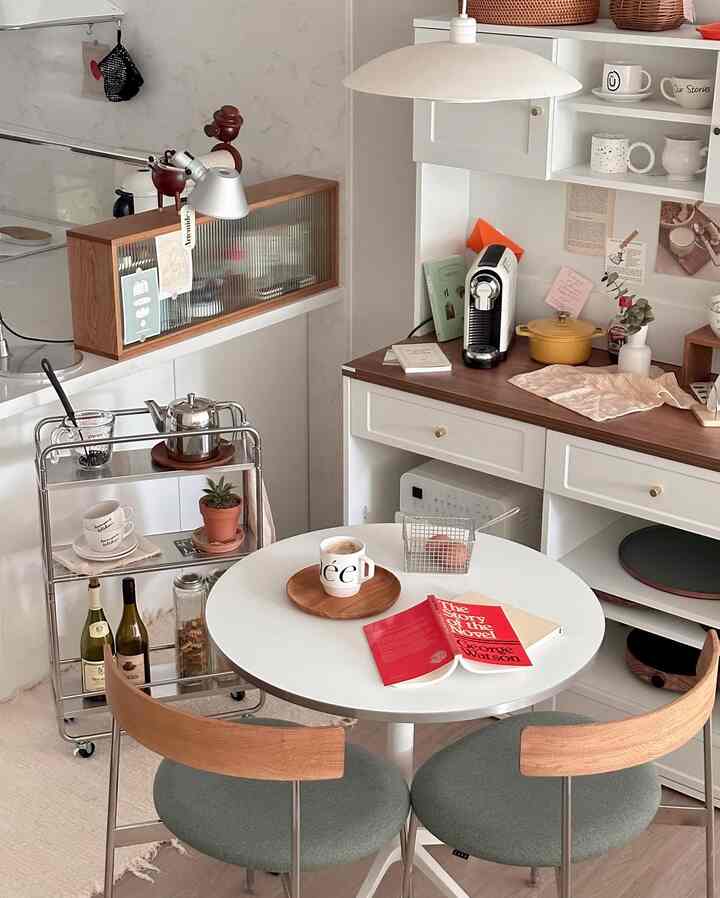 白と木目調が調和したキッチンのホームカフェゾーン、丸テーブルと椅子、ステンレス製キッチンワゴンが配置された雰囲気のある空間