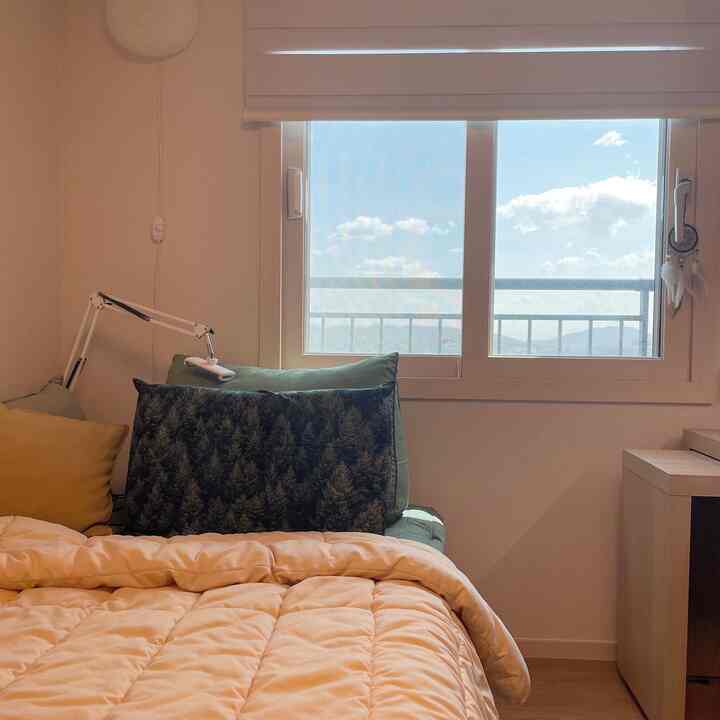 Beige and white toned bedroom space featuring bed with pillows by a window, creating a cozy atmosphere