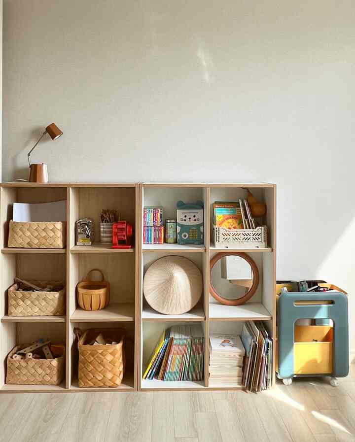 ベージュトーンの子供部屋の壁、ナチュラルな木製本棚と整理された収納ボックスが配置された清潔感のある空間