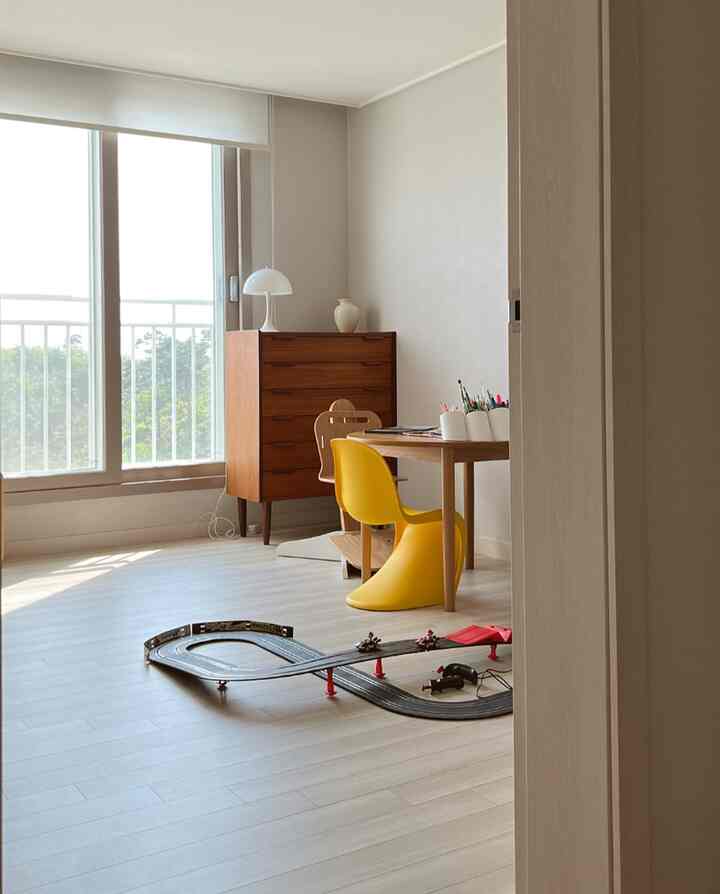 ナチュラルモダンな子供部屋、黄色いパントンチェアとおもちゃのカーレーストラックが配置された清潔感のある空間