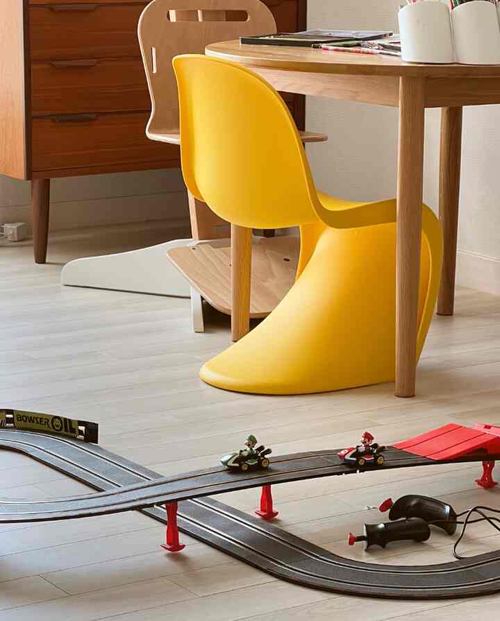明るくナチュラルな木目調と黄色い椅子がある子供部屋、スーパーマリオの玩具レーストラックが配置された遊びのある空間