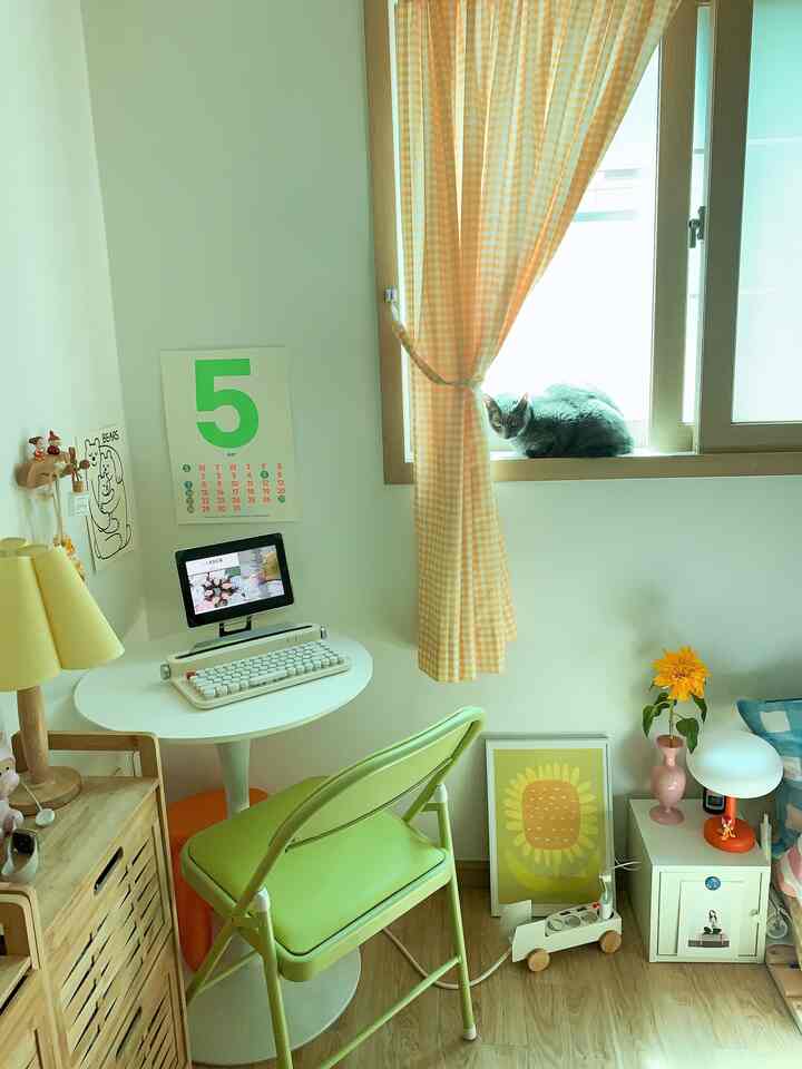 Cozy compact studio home office with yellow accents and wood tones featuring a round table, folding chair, and a cat on the window sill
