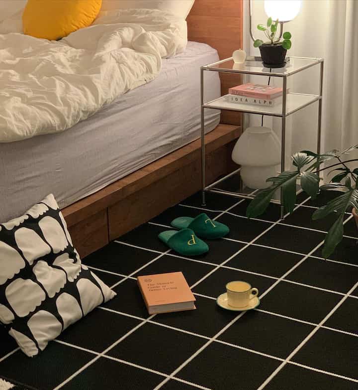 Black and white toned bedroom featuring wood tone bed, rug, plants, and a mood lamp creating a cozy atmosphere