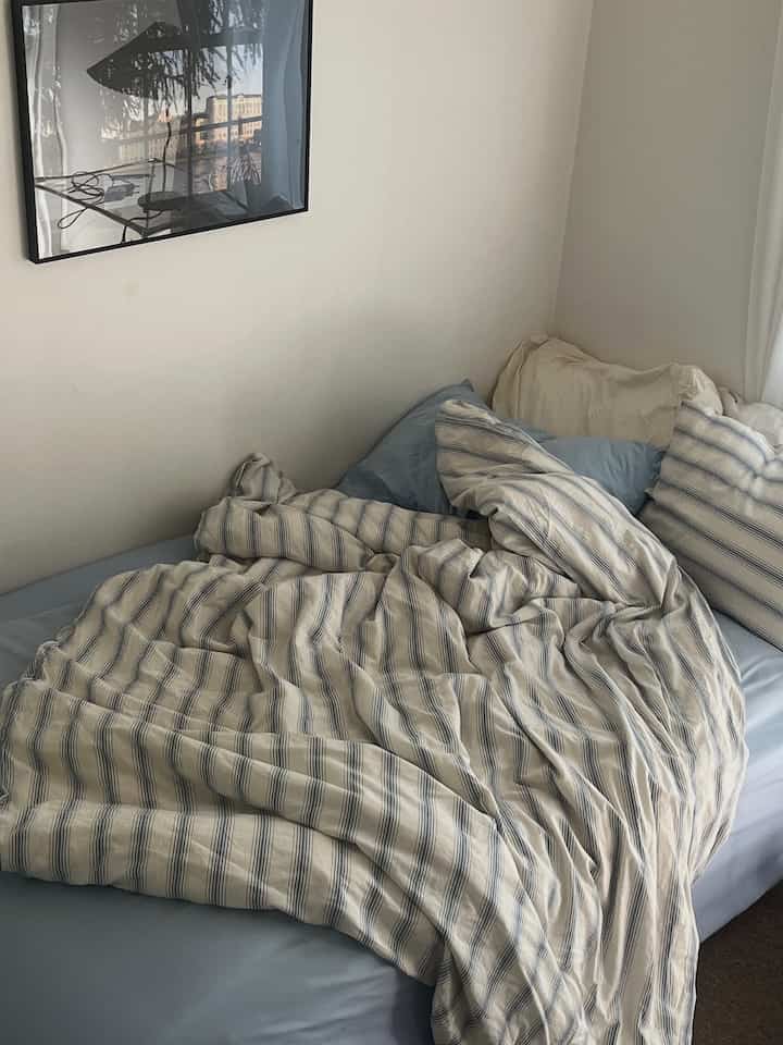 A simple modern bedroom with white and blue tones, featuring striped bedding and various pillows