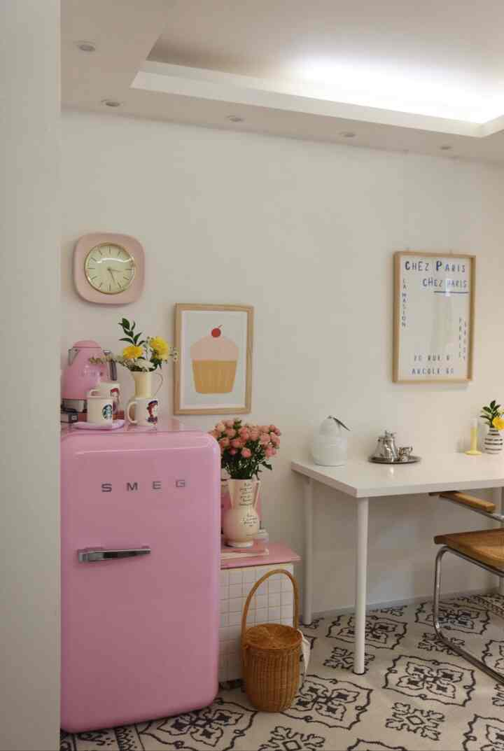 Bright white-toned kitchen and living space featuring a pink retro fridge and patterned rug in a cozy cafe-style interior