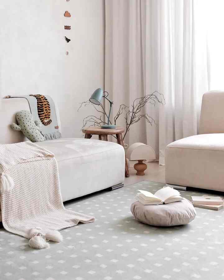 A natural-toned living room featuring beige sofas, a wooden stool with a table lamp, and white curtains for a cozy atmosphere