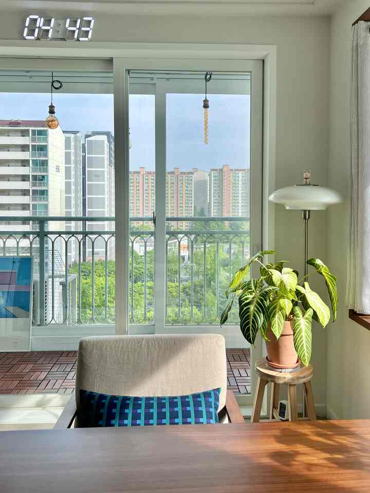 White and wood tone living room with balcony view, featuring wooden table and green plant in a natural setting