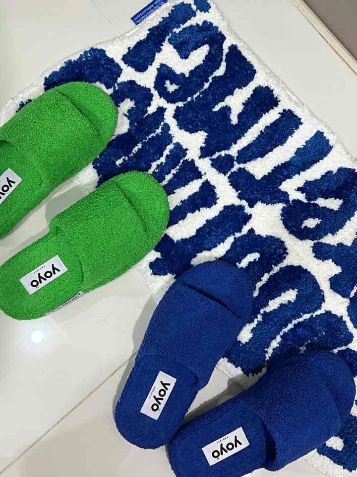 Bathroom space featuring blue and white bath mat with blue and green indoor slippers arranged on tiled floor
