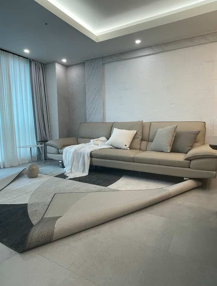 アイボリーとベージュのトーンでまとめられたモダンなリビング、ベージュのソファとカーペットが配置された広々とした清潔感のある空間