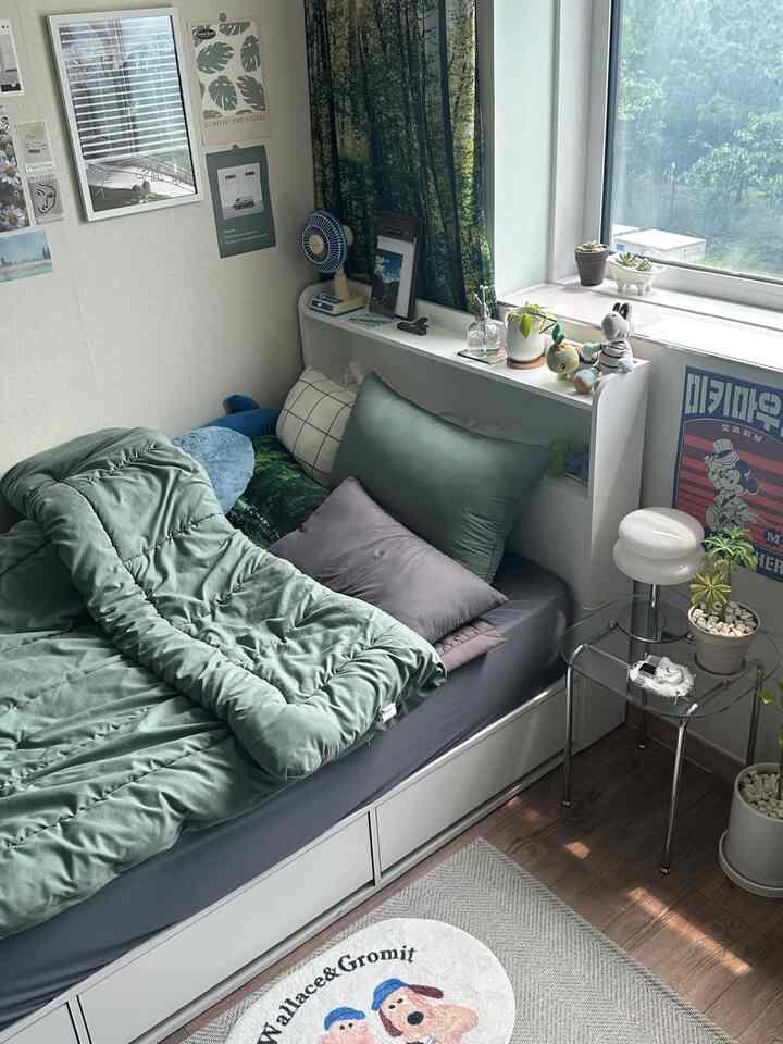 緑の寝具と植物が配置されたコンパクトで居心地の良い寝室、整った収納と自然な雰囲気のインテリア