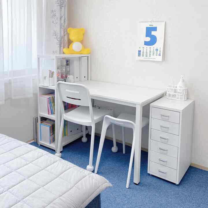 White and blue toned kids' room featuring a clean desk with chairs, storage cabinet, and a May calendar, creating a bright, organized space