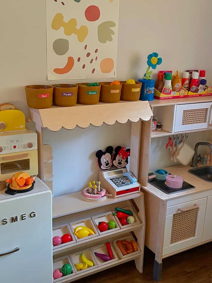Natural tone kids' room featuring wooden toy kitchen and colorful pretend play items in a cozy setting