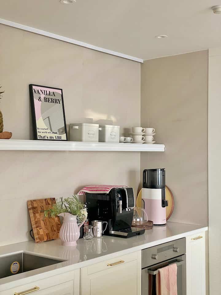 ホワイトとピンク色調のキッチン、コーヒーマシンやキッチン家電が整然と配置された自然な雰囲気のインテリア