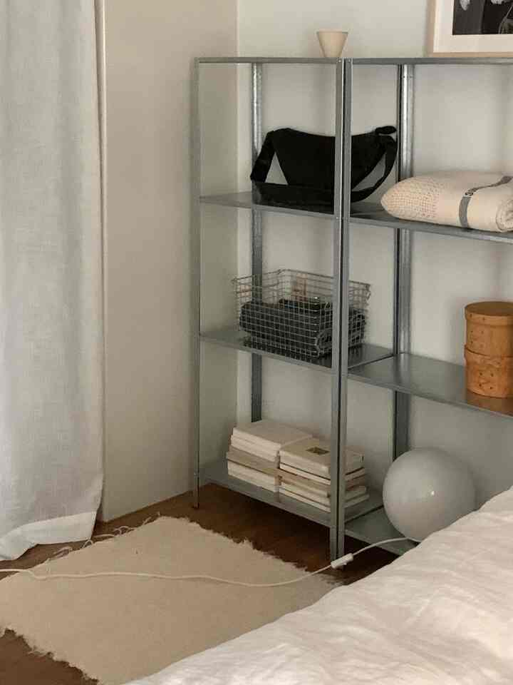 Natural tone bedroom space with metal shelving and beige rug arranged in a clean atmosphere